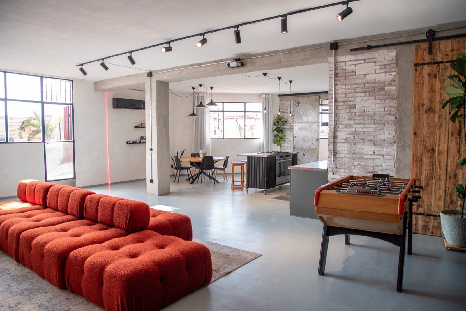 Salón interior de Ático Eme con sofá terracota, futbolín y cocina abierta